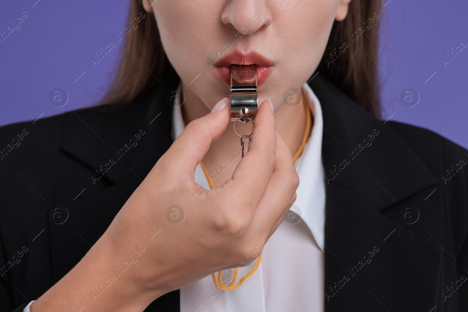 Photo of Woman blowing whistle on purple background, closeup