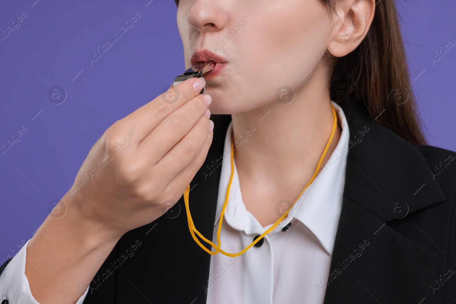 Photo of Woman blowing whistle on purple background, closeup