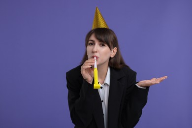 Woman in party hat with blower on purple background