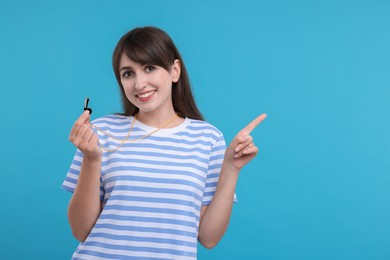 Happy woman with whistle on light blue background, space for text