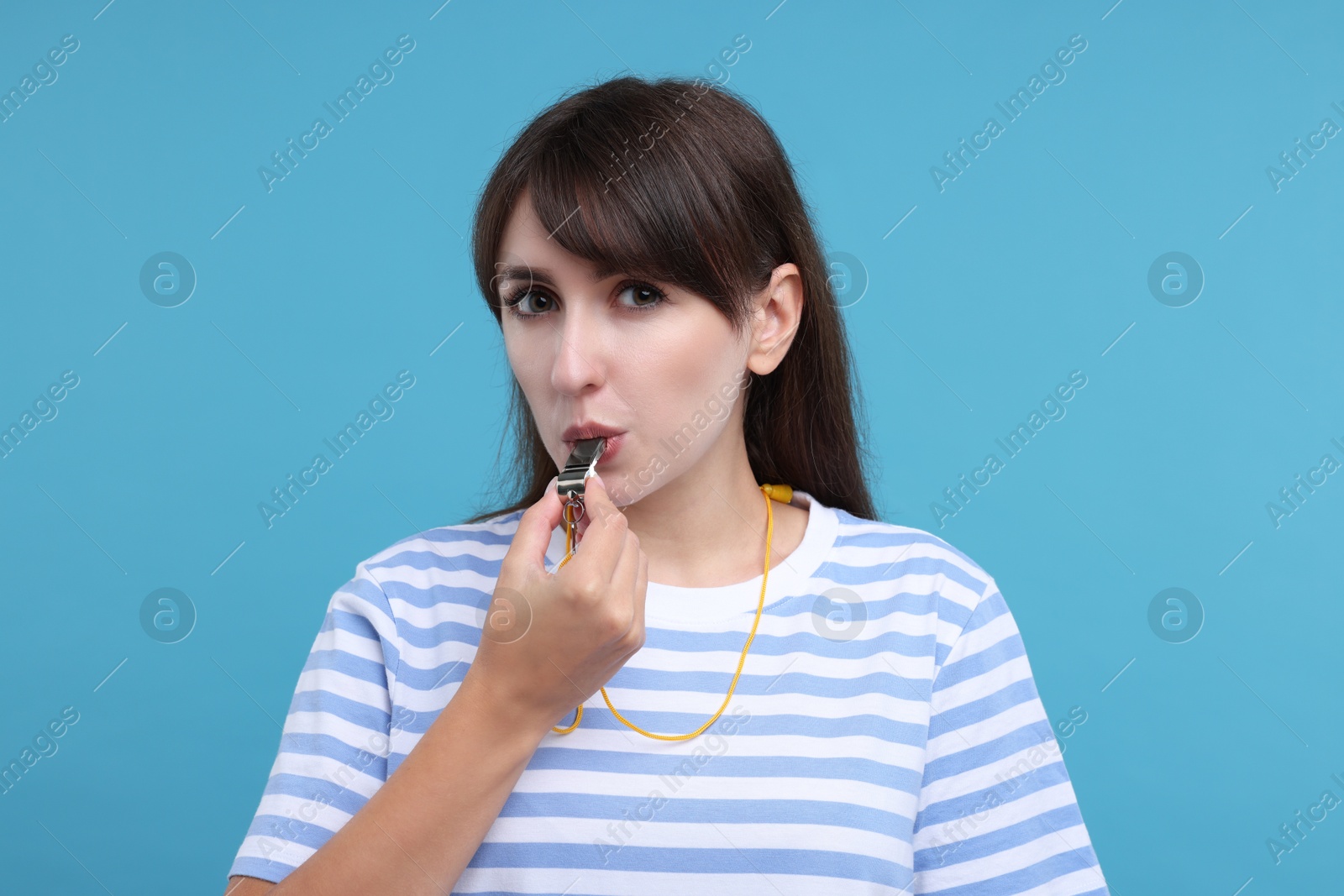 Photo of Woman blowing whistle on light blue background