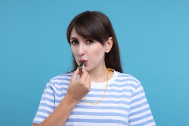 Woman blowing whistle on light blue background