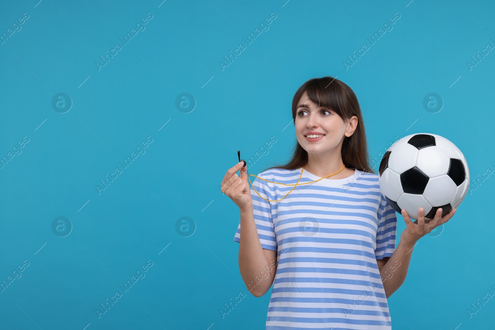 Photo of Happy woman with whistle and soccer ball on light blue background, space for text