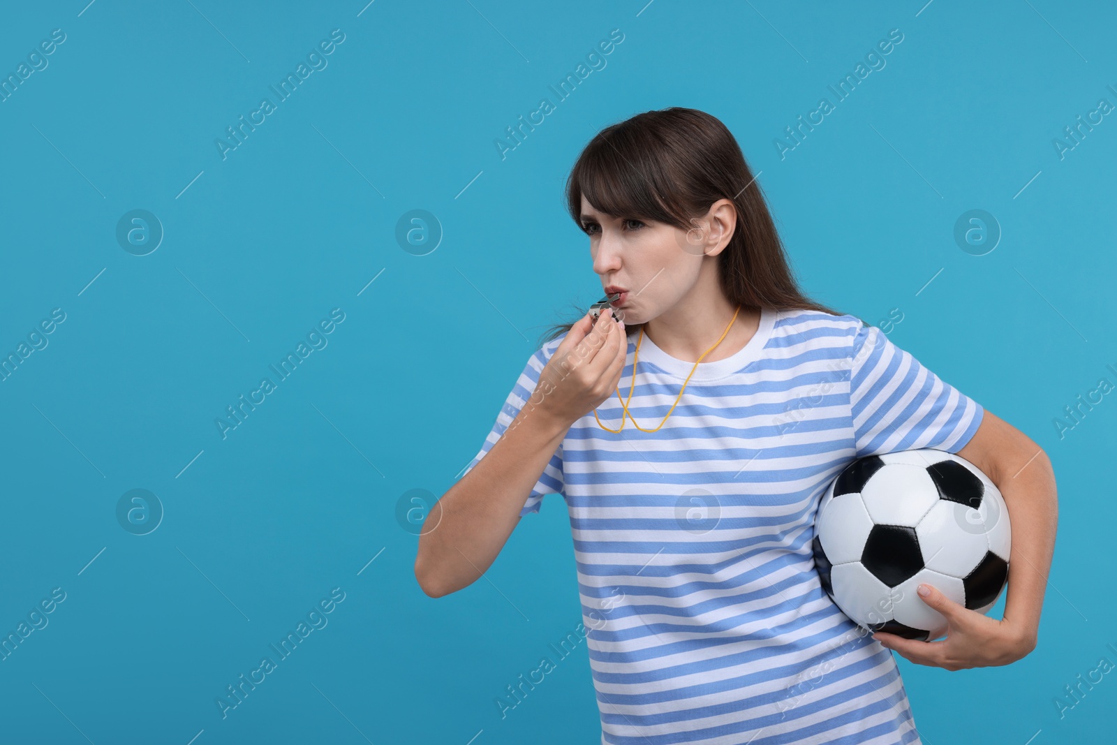 Photo of Woman with soccer ball blowing whistle on light blue background, space for text