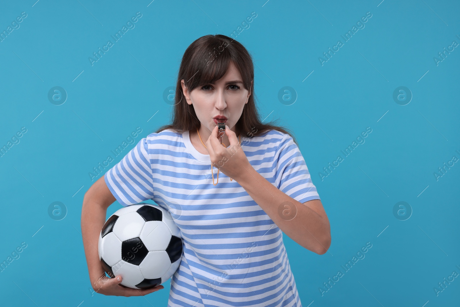 Photo of Woman with soccer ball blowing whistle on light blue background