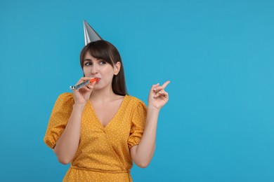 Photo of Woman in party hat with blower on light blue background, space for text