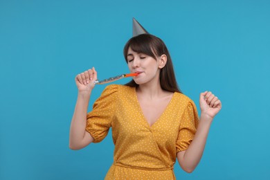 Photo of Woman in party hat with blower on light blue background