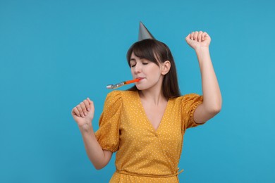 Woman in party hat with blower on light blue background