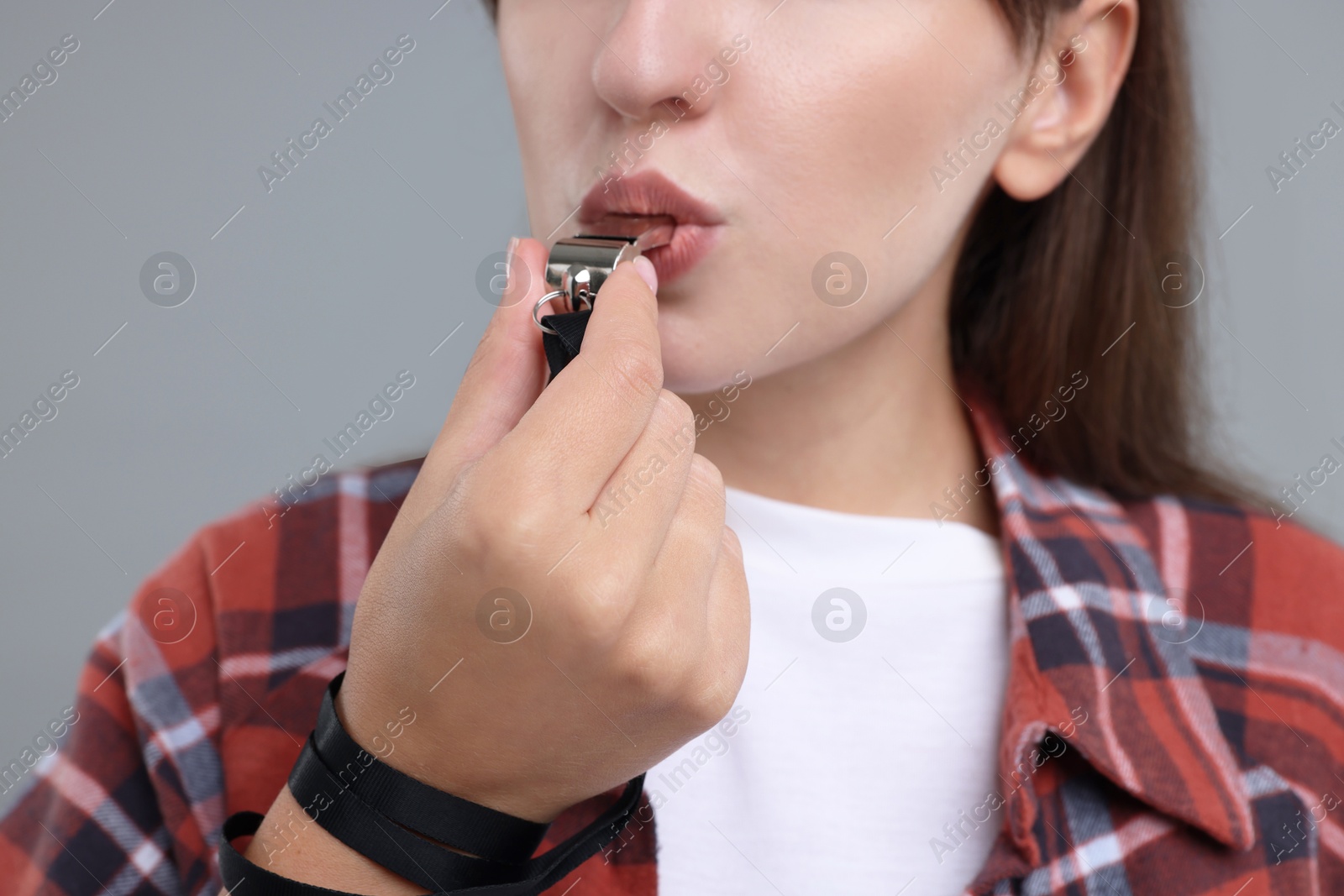 Photo of Woman blowing whistle on grey background, closeup