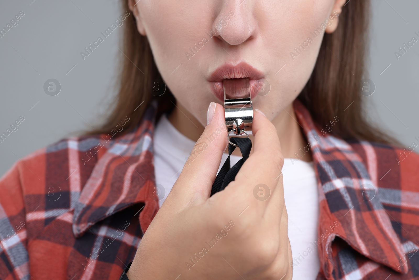 Photo of Woman blowing whistle on grey background, closeup