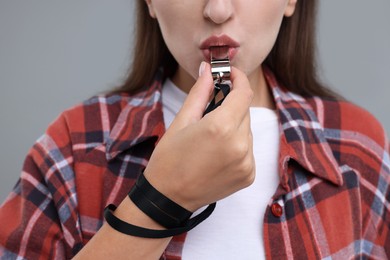 Woman blowing whistle on grey background, closeup