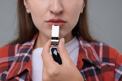 Woman with whistle on grey background, closeup