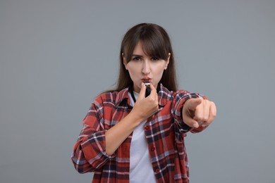 Photo of Young woman blowing whistle on grey background