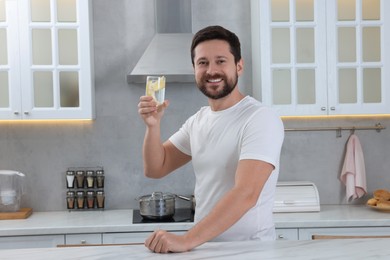 Happy man holding glass of water with lemon in kitchen