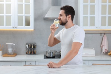 Handsome man drinking water with lemon in kitchen