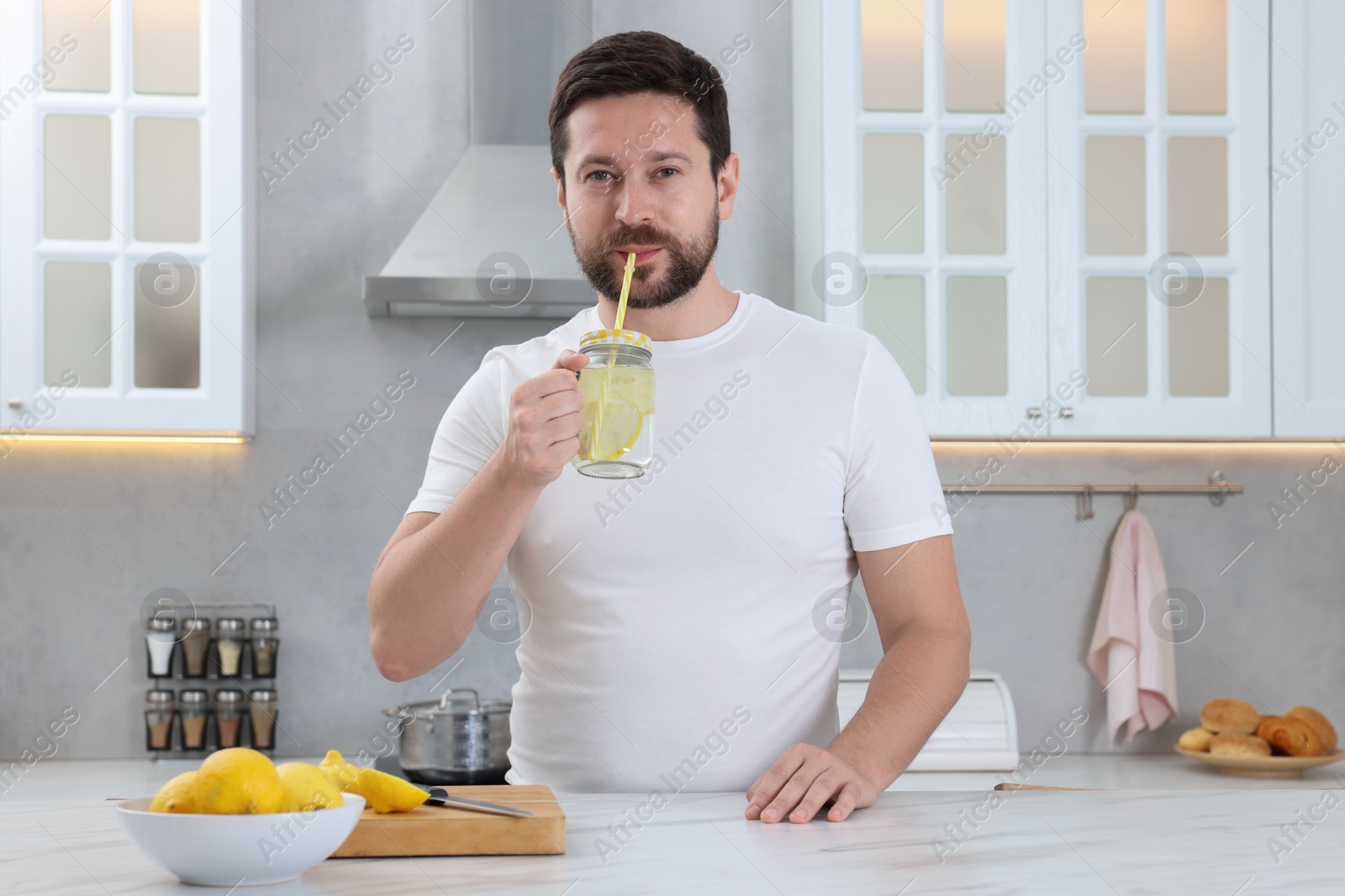 Photo of Handsome man drinking water with lemon in kitchen