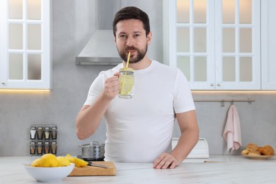 Handsome man drinking water with lemon in kitchen