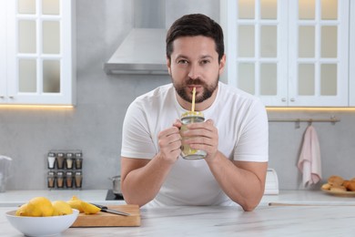 Handsome man drinking water with lemon in kitchen