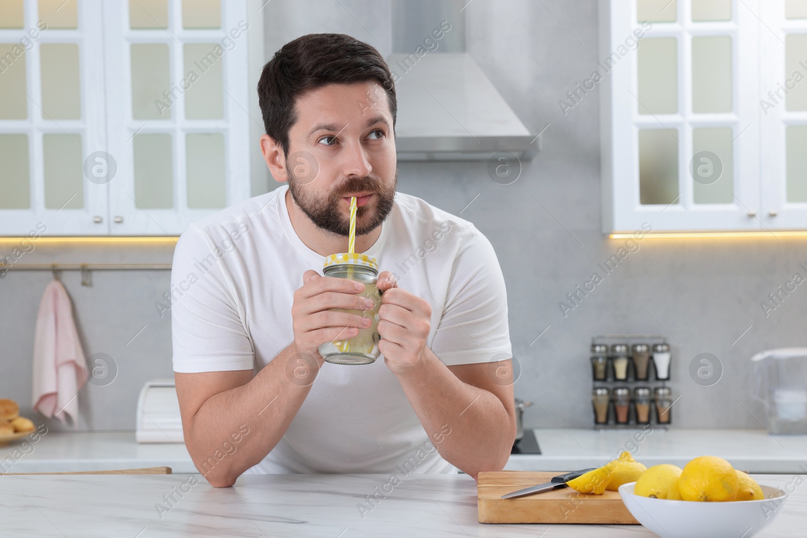 Photo of Handsome man drinking water with lemon in kitchen