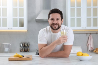 Photo of Happy man holding glass of water with lemon in kitchen