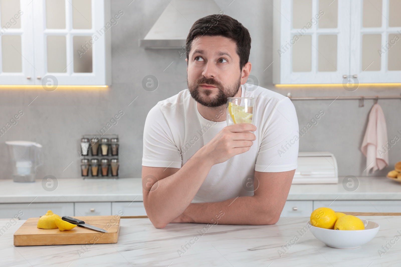 Photo of Handsome man holding glass of water with lemon in kitchen