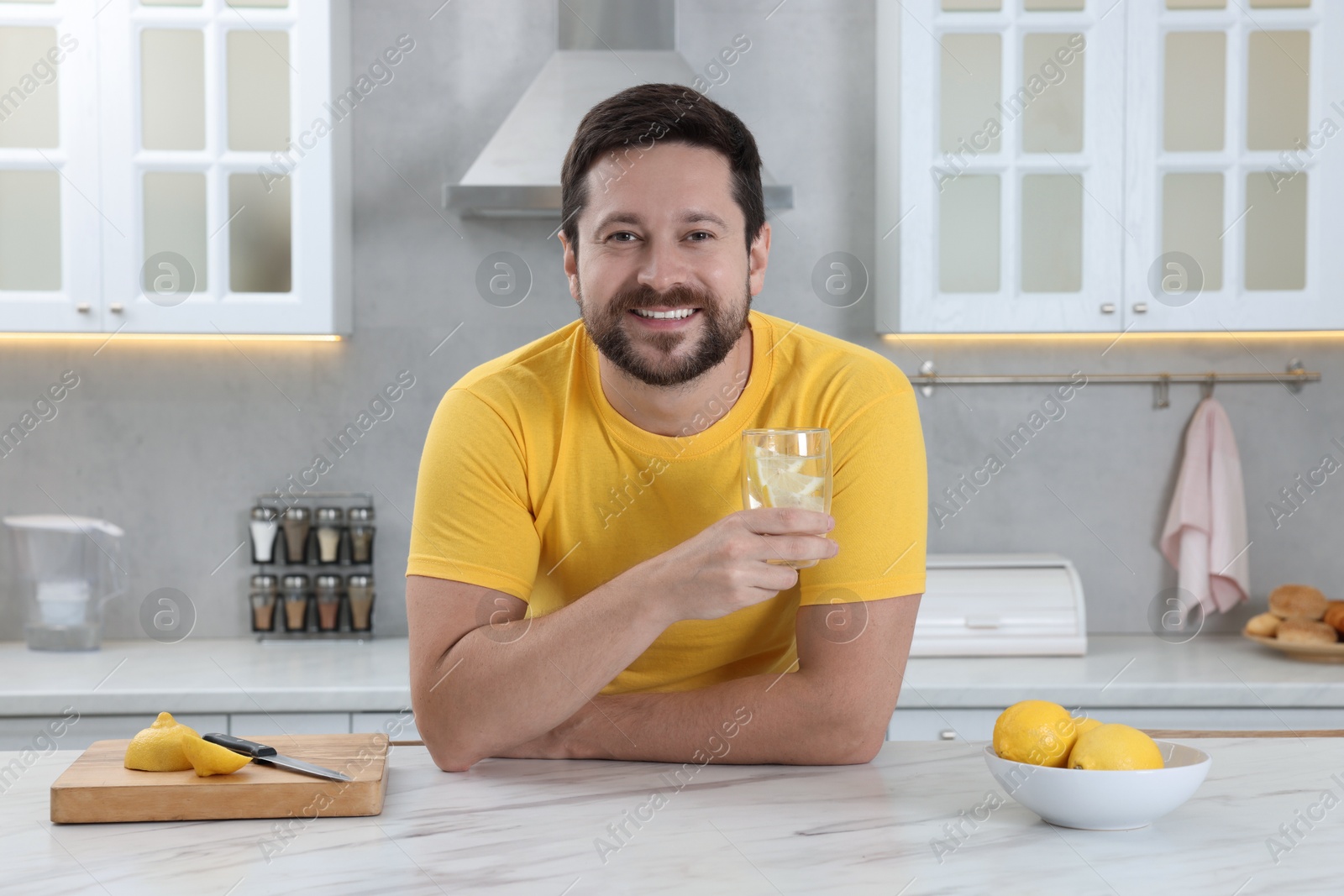 Photo of Happy man holding glass of water with lemon in kitchen