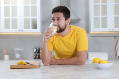 Handsome man drinking water with lemon in kitchen