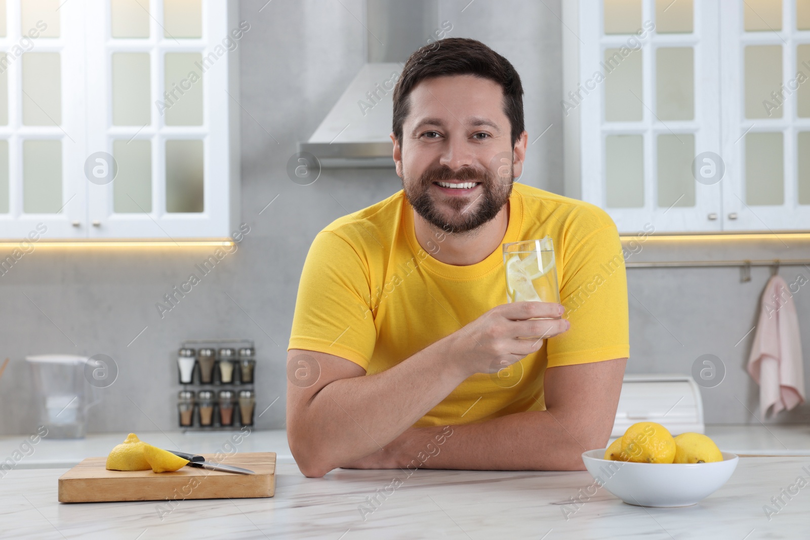 Photo of Happy man holding glass of water with lemon in kitchen