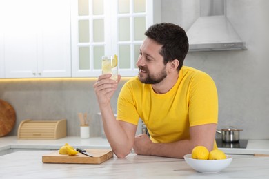 Happy man holding glass of water with lemon in kitchen