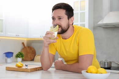 Photo of Handsome man drinking water with lemon in kitchen