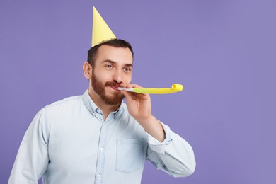 Man in party hat with blower on purple background, space for text