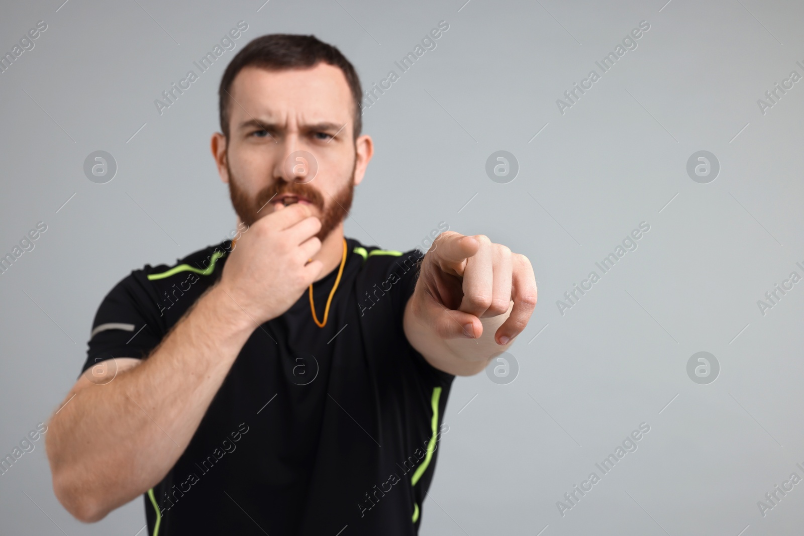 Photo of Young man blowing whistle on grey background, space for text