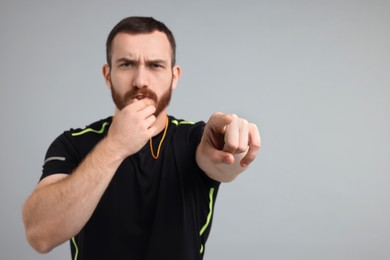 Young man blowing whistle on grey background, space for text