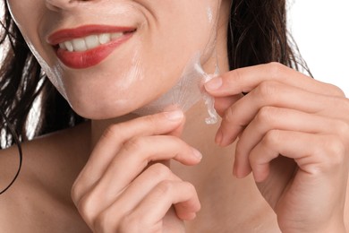 Smiling woman peeling off face mask on white background, closeup