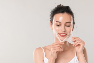 Photo of Smiling woman peeling off face mask on light grey background. Space for text