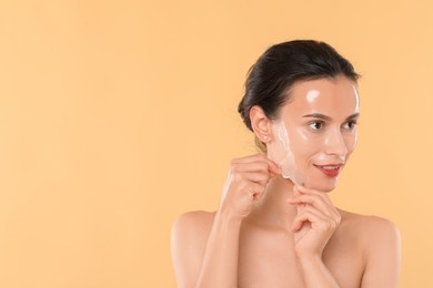 Beautiful woman peeling off face mask on beige background. Space for text