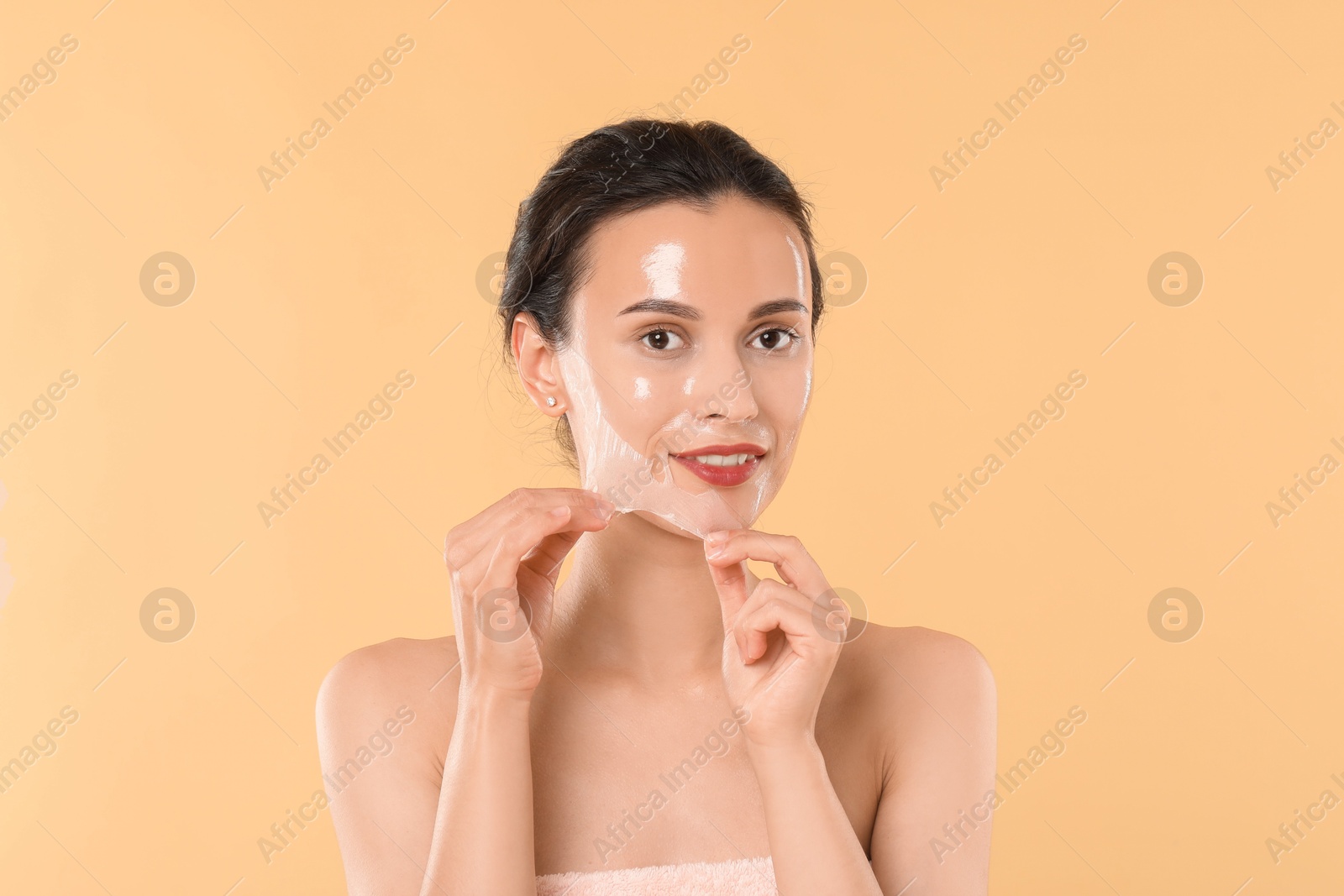 Photo of Smiling woman peeling off face mask on beige background