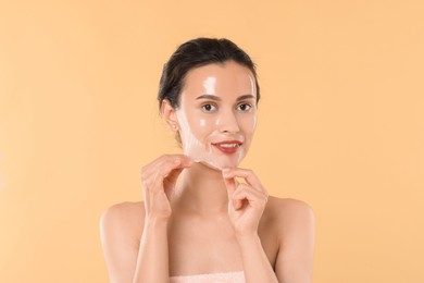 Smiling woman peeling off face mask on beige background