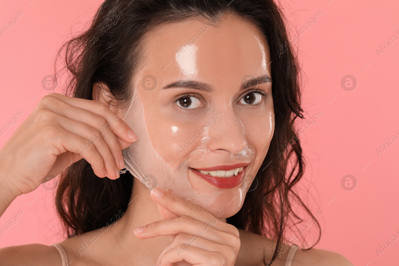 Photo of Smiling woman peeling off face mask on pink background, closeup