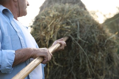 Senior man pitching hay on farmland, closeup