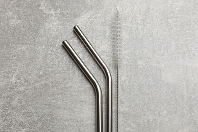 Photo of Metal drinking straws and cleaning brush on gray textured table, top view