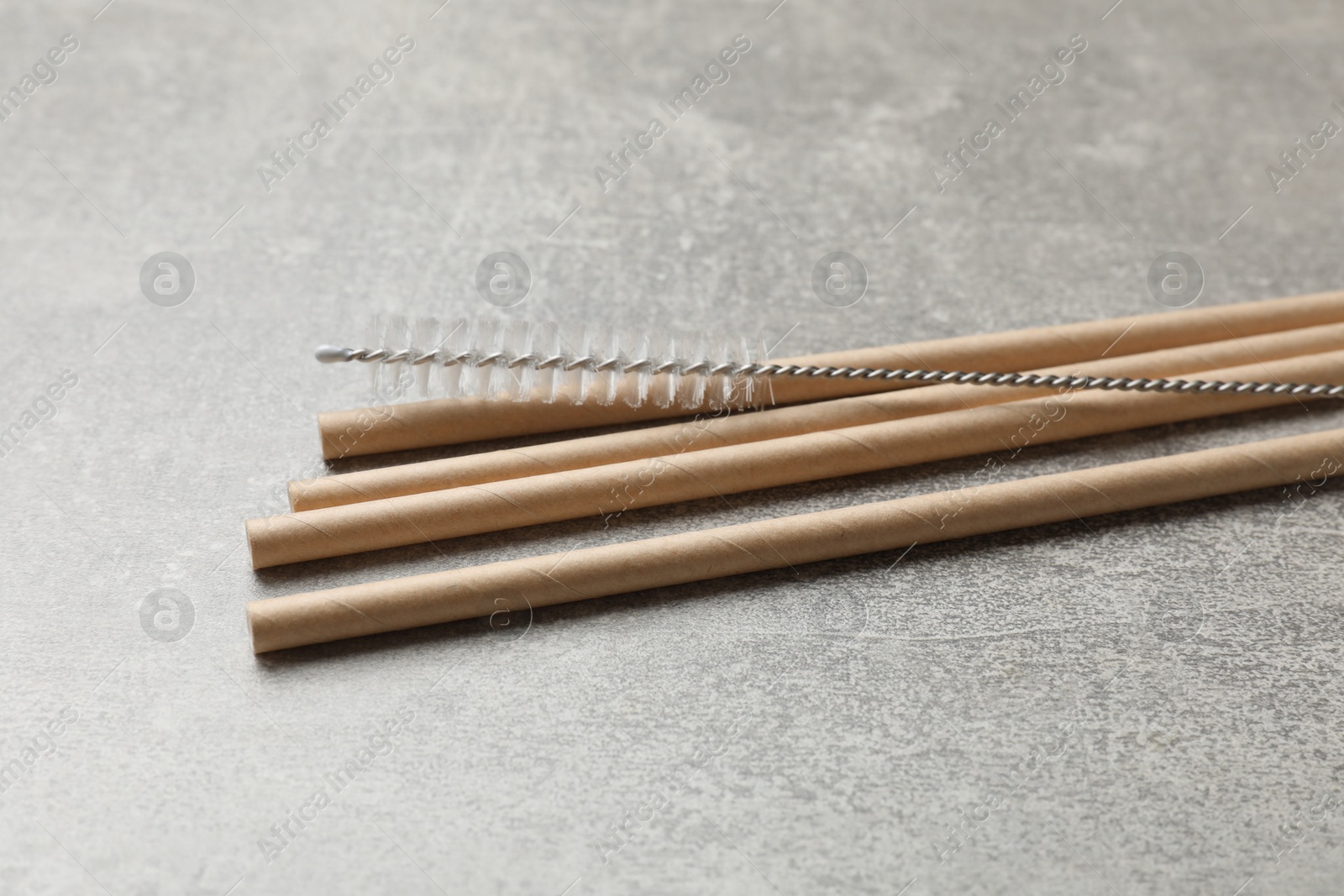 Photo of Bamboo drinking straws and cleaning brush on gray textured table, closeup