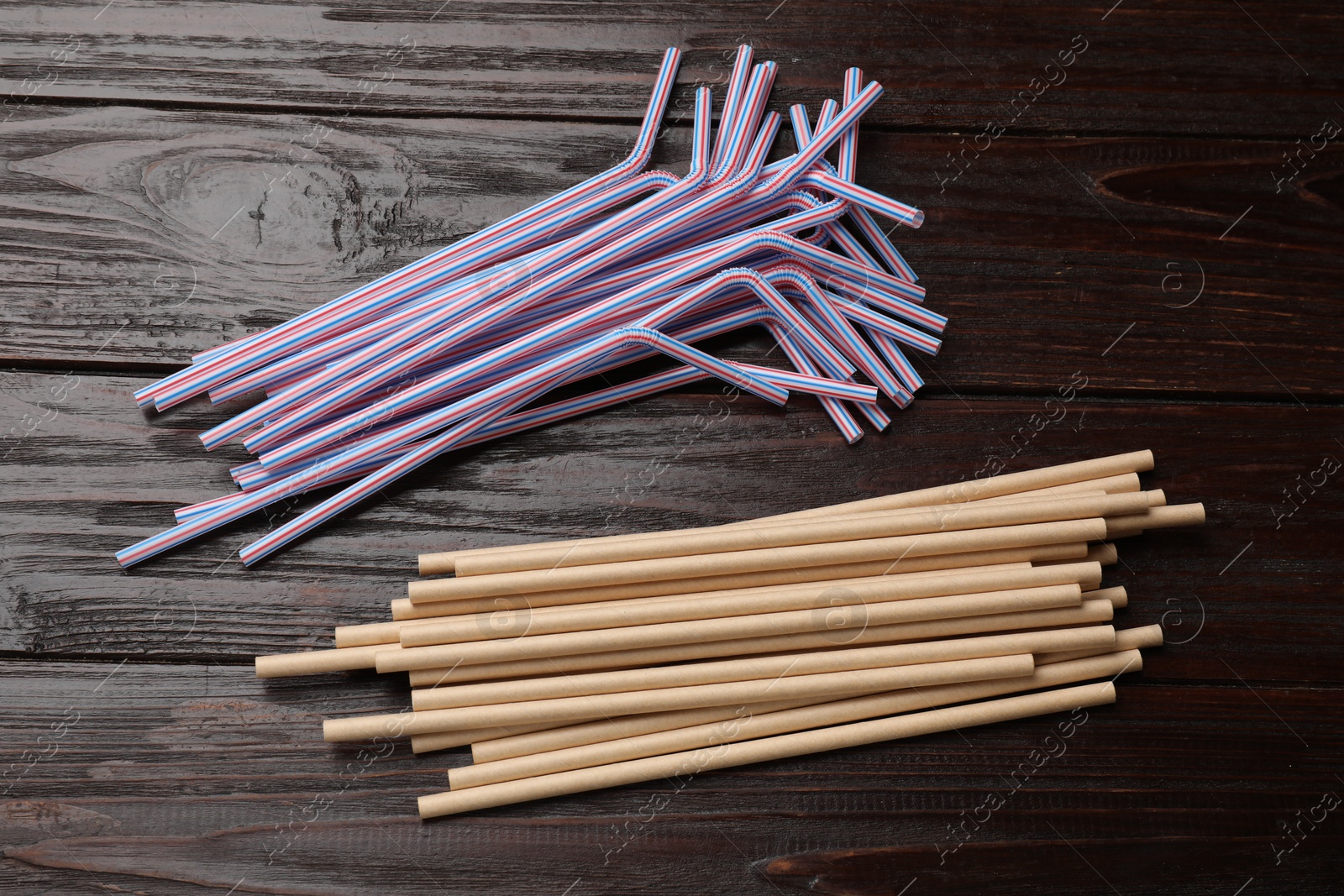 Photo of Plastic and bamboo drinking straws on wooden table, flat lay