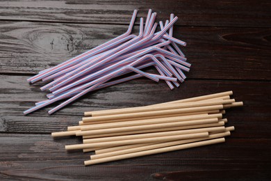 Photo of Plastic and bamboo drinking straws on wooden table, flat lay