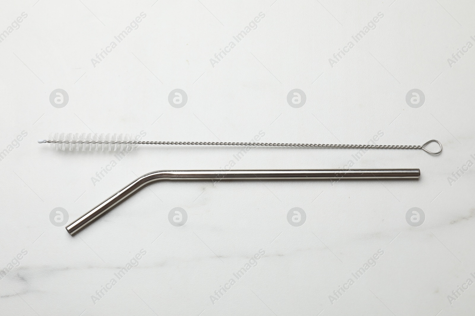 Photo of Metal drinking straw and cleaning brush on light marble table, flat lay