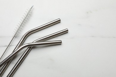 Photo of Metal drinking straws and cleaning brush on light marble table, flat lay. Space for text