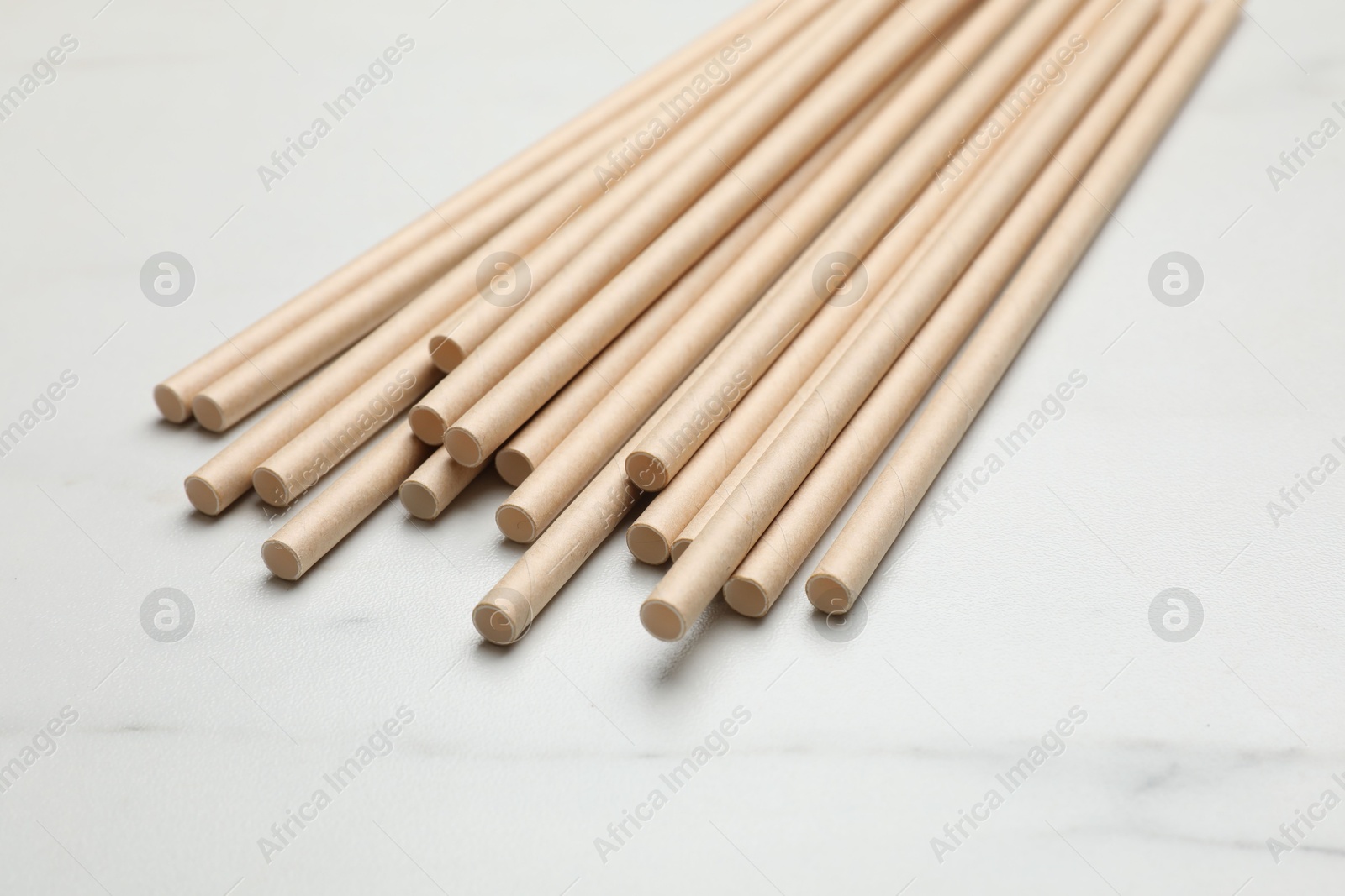 Photo of Bamboo drinking straws on light marble table, closeup