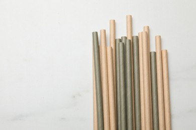 Photo of Bamboo drinking straws on light marble table, top view. Space for text