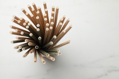 Photo of Bamboo drinking straws on light marble table, top view. Space for text