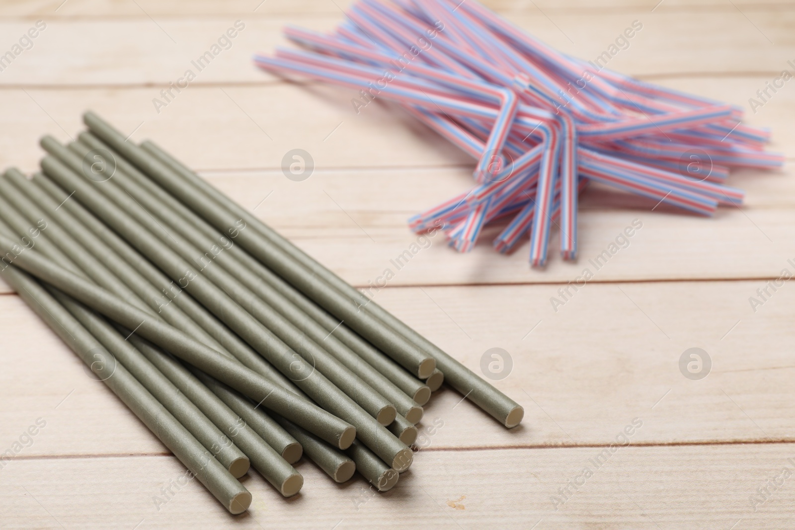 Photo of Bamboo and plastic drinking straws on wooden table, closeup